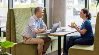 Kaksi henkilöä keskustelee kannettavien tietokoneiden ääressä kahvilassa