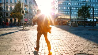 Kadulla kulkee henkilö, johon osuu auringonsäteitä. 