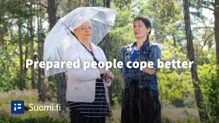 Two women - one is under umbrella and the other one is not